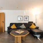 Schwarzes Sofa mit gelben und karierten Kissen, Holztisch und Stehlampe im Wohnzimmer.