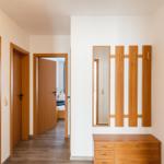 Flur mit Holzmöbeln, Spiegel und Garderobe. Tür zum Schlafzimmer sichtbar.