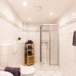 Badezimmer mit Dusche, Toilette und Waschbecken. Wände und Boden sind mit Fliesen verkleidet.