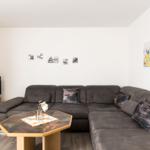 Ein Wohnzimmer mit grauem Sofa, Holztisch und Fernseher an der Wand.