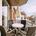 Terrasse mit Tisch, vier Stühlen und geschlossenem Sonnenschirm. Blick auf Dächer und Gebäude.