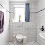 Badezimmer mit Toilette, Waschbecken und Fenster mit Vorhang.