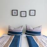Zwei Betten mit Streifenbetten und Kissen, Wand mit drei Bildern und Nachttischlampen.