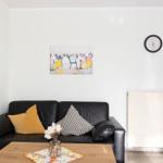 Schwarzes Sofa mit Kissen, Tisch, Wanduhr und Bild an der Wand.