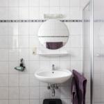 Badezimmer mit Dusche, Waschbecken und runden Spiegel