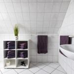 Badezimmer mit weißen Fliesen, Handtuchhalter und Regal mit Handtüchern.