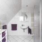 Badezimmer mit Dusche, Waschbecken und Dachneigung. Lila Handtücher und Pflanze.