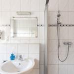 Badezimmer mit Dusche, Waschbecken und Spiegel. Weiße Fliesen mit blauer Zierleiste.