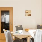 Esszimmer mit Tisch, Stühlen und Wandbildern. Tür führt in Wohnbereich.