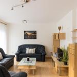 Wohnzimmer mit zwei schwarzen Ledersofas, Glas-Tisch und Holzmöbeln.