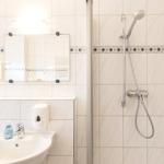 Badezimmer mit Dusche, Waschbecken und Spiegel an der Wand.