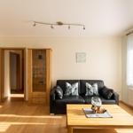 Wohnzimmer mit schwarzer Couch, Holztisch und Glasvitrine.