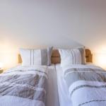 Zwei Betten mit Kissen und Bettwäsche unter einer schrägen Decke mit Nachttischen und Lampen.
