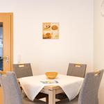 Esszimmer mit Tisch, vier Stühlen und Wandbild mit Muscheln.