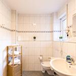 Badezimmer mit Toilette, Waschbecken und Handtuchständer. Fliesenwand mit blauer Zierleiste.