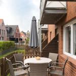 Terrasse mit Tisch, Stühlen und Schirm. Hinterhof mit Holzzaun und Grünflächen.