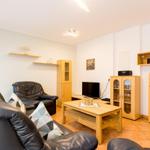 Wohnzimmer mit Ledersofa, Holztisch und Küchenschränken an der Wand.