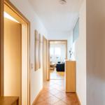 Flur mit Holztüren und Terrakottboden, Blick in Wohnzimmer mit Sofa und Fenster.