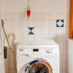 Waschmaschine in einem Raum mit Fliesenwand und rotem Wasserhahn.