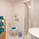 Badezimmer mit Dusche, Toilette und Waschbecken. Holzregal mit blauen Handtüchern.