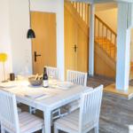 Esstisch mit vier Stühlen, Flur mit Holztreppe und weiße Wände.
