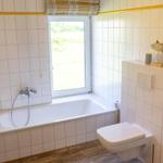 Badezimmer mit Badewanne, Fenster und Toilette. Wandfliesen und Holzboden.