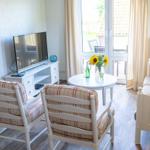 Wohnzimmer mit Sofa, zwei Stühlen, TV und Tisch mit Sonnenblumen.
