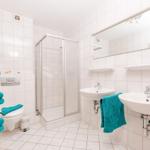 Badezimmer mit Dusche, zwei Waschbecken und Toilette. Türkis Handtücher und Spiegelschrank.