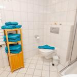 Badezimmer mit Toilette, Dusche und Holzregal mit blauen Handtüchern.