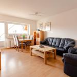 Wohn- und Essbereich mit Holzmöbeln, Ledersofa und TV. Durchgang zum Balkon.