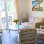 Wohnzimmer mit Sofa, zwei Stühlen, Tisch und Fernseher. Durchgang zur Terrasse.