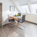 Essbereich mit Tisch, Stühlen und Schrank unter Dachschrägen mit Fenstern.