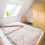 Schlafzimmer mit Dachfenster, Bett, Kleiderschrank und Stuhl.