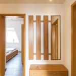 Eingangsbereich mit Holzgarderobe, Spiegel und Schreibtisch. Links Schlafzimmer, rechts Wohnzimmer.
