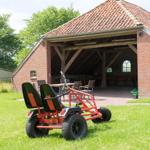 Roter Gartengabelwagen steht auf Gras vor einem Backstein-Stall mit Holzkonstruktion.