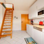Küche mit weißen Schränken, rotem Toaster und Holztreppe zur oberen Etage.