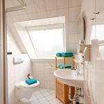 Badezimmer mit Toilette, Waschbecken und Dachfenster. Türkis Handtücher und Holzregal.