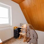 Dachgeschoss mit Holzdecke, Stiege und Fenster. Kinderhochstuhl und Pflanze sichtbar.