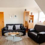 Wohnzimmer mit schwarzer Ledercouch, Glas-Tisch und Holzmöbeln unter Dachschrägen.