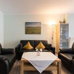 Wohnzimmer mit schwarzen Ledersofas, Holztisch und Wandbild.