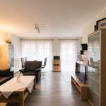 Wohnzimmer mit Sofa, Sessel, Couchtisch und Fernseher. Hintergrund: Essbereich mit Tisch und Stühlen.