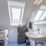 Badezimmer mit Waschmaschine, Spiegel und Dachfenster. Fliesen und blaue Bodenfliesen.