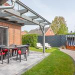 Terrasse mit Tisch, Stühlen und Sonnenschutz. Garten mit Liegen und Strandkorb.