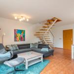 Wohnbereich mit Sofa, Sessel und Treppe zur oberen Etage.