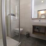 Badezimmer mit Dusche, Toilette und Waschbecken mit beleuchtetem Spiegel.