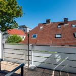 Terrasse mit Gartenzaun und Blick auf Dach mit Schornsteinen und Fenstern.