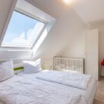 Schlafzimmer mit Dachfenster, Bett und Kinderbett. Roter Stuhl im Flur.