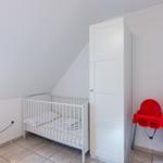 Kinderzimmer mit Babybett, Kleiderschrank und roter Hochstuhl.