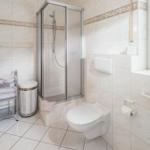 Badezimmer mit Dusche, Toilette und Fenster mit Pflanze.