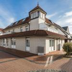 Ein zweistöckiges Haus mit Ziegeldach und weißem Klinkerfassade. Vorhof mit Pflanzen und gepflastertem Boden.